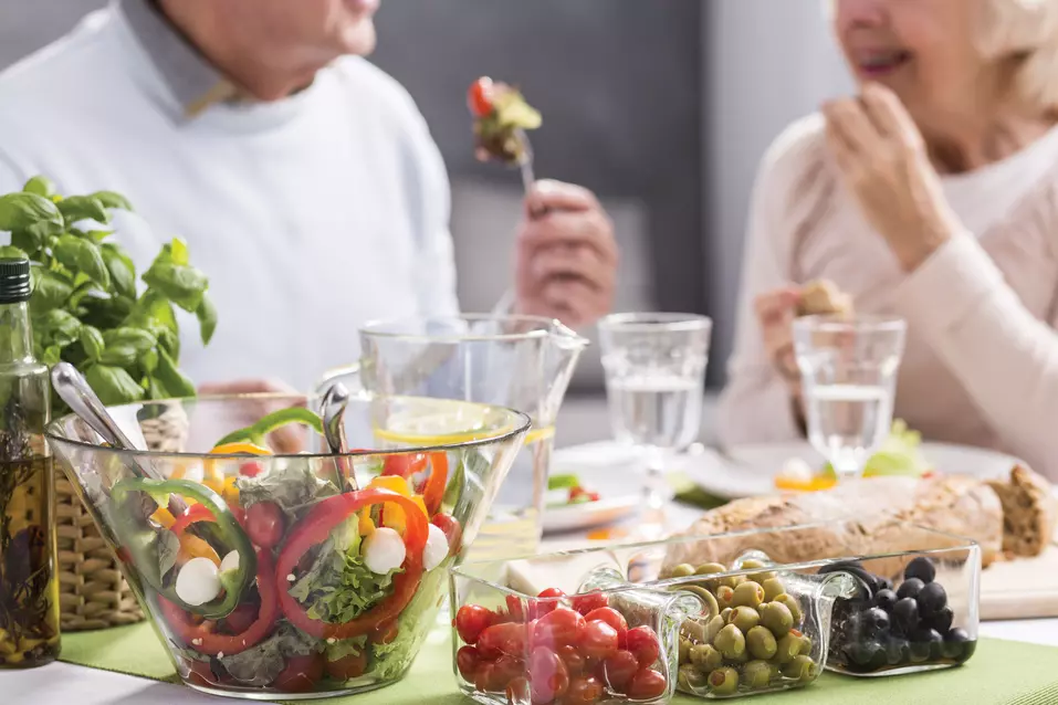 Senior couple are having fresh salads, olives and whole wheat bread as a meal / Le couple de seniors prend comme repas des salades fraîches, des olives et du pain de blé entier
