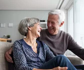 Senior couple in a couch happily laughing while looking into each others' eye / Couple de seniors dans un canapé, riant joyeusement en se regardant dans les yeux