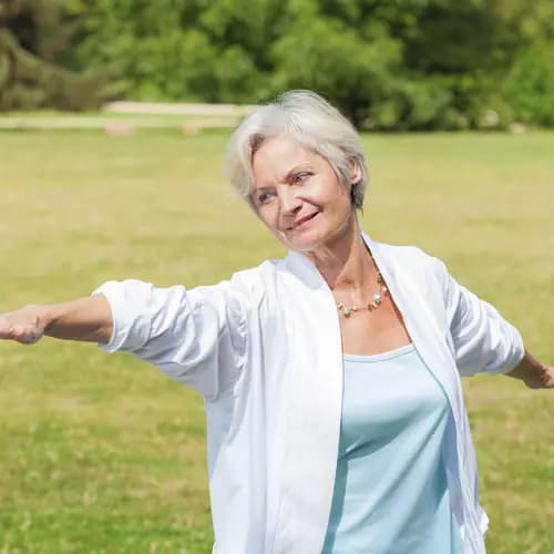 Senior woman practicing tai chi with her arms stretched on a field of grass