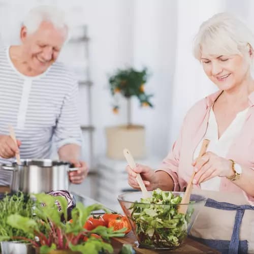 senior couple preparing a meal and salad in a kitchen / couple âgé préparant un repas et une salade dans une cuisine