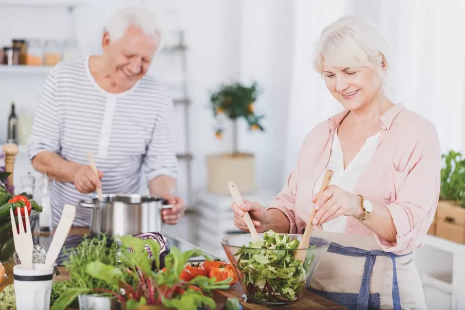 senior couple preparing a meal and salad in a kitchen / couple âgé préparant un repas et une salade dans une cuisine