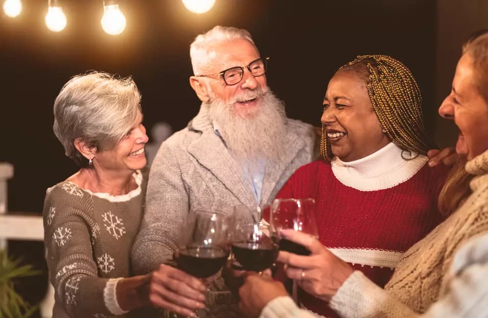 A group of seniors are toasting their wine glasses with a big joyous smiles during a holiday party / Un groupe de personnes âgées trinquent avec un grand sourire joyeux lors d'une fête de fin d'année.