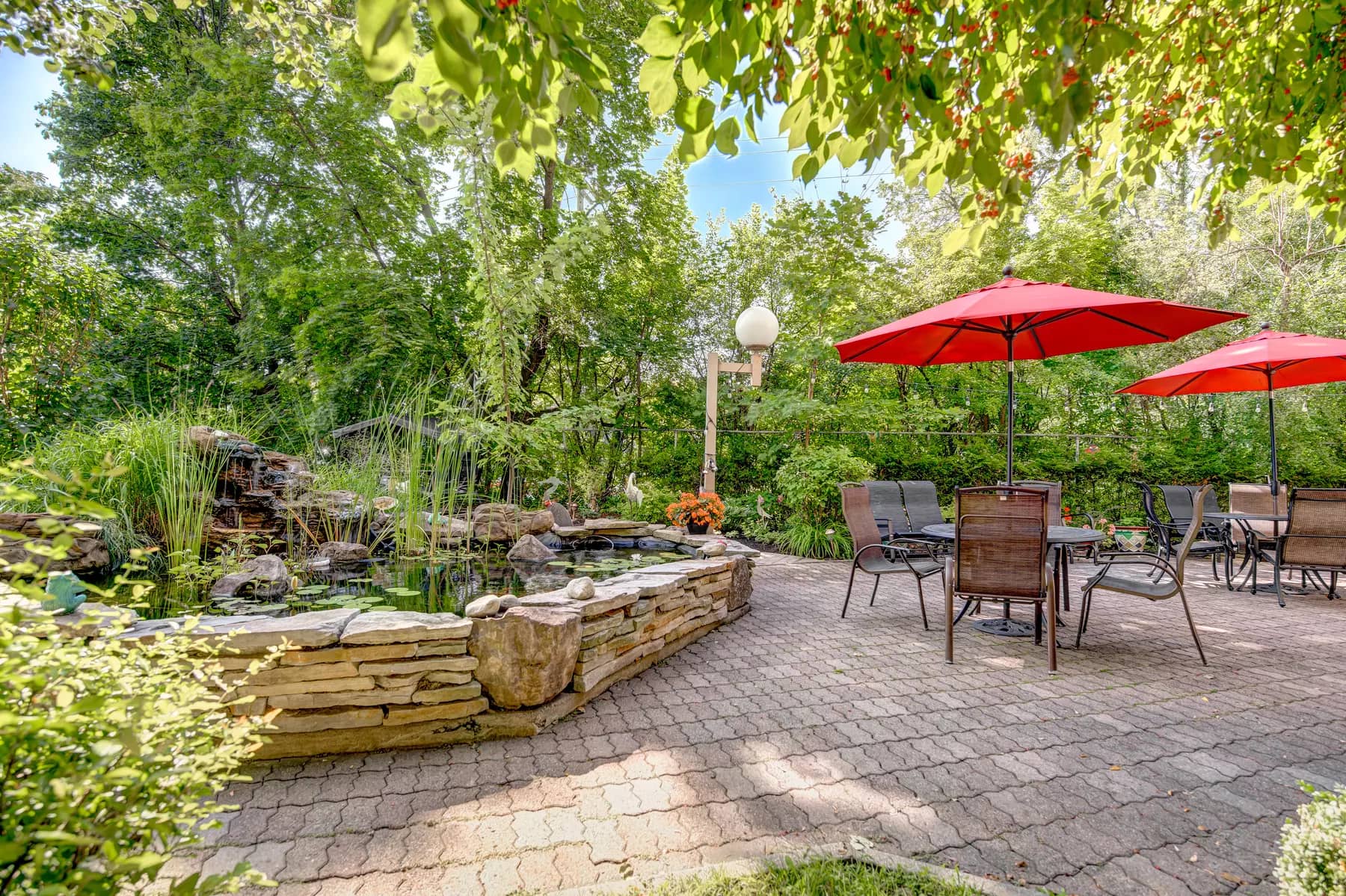 Salon extérieur au bord d'un étang avec table parasol chez Chartwell Manoir Kirkland / Outdoor sitting area beside a pond with a parasol table at Chartwell Manoir Kirkland